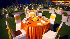 An outdoor banquet hall at the lawn of The Bristol Hotels, Gurgaon featuring several sets of tables and chairs with fabrics and other designing materials.