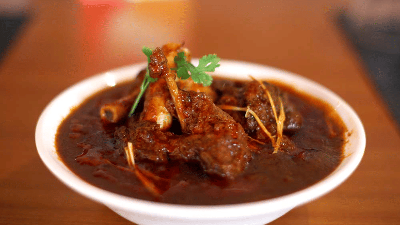 A meat dish in a deep coloured gravy garnished with coriander placed in a bowl on a table at The Bristol Hotel, best choice for a corporate outing in Gurgaon.