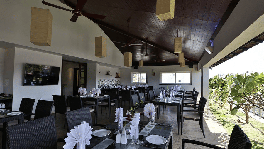 The spacious covered rooftop dining area in Tree Top Restaurant with arranged table settings, folded napkins, and outdoor balcony plants at Temple Tree Hotel, Bangalore.
