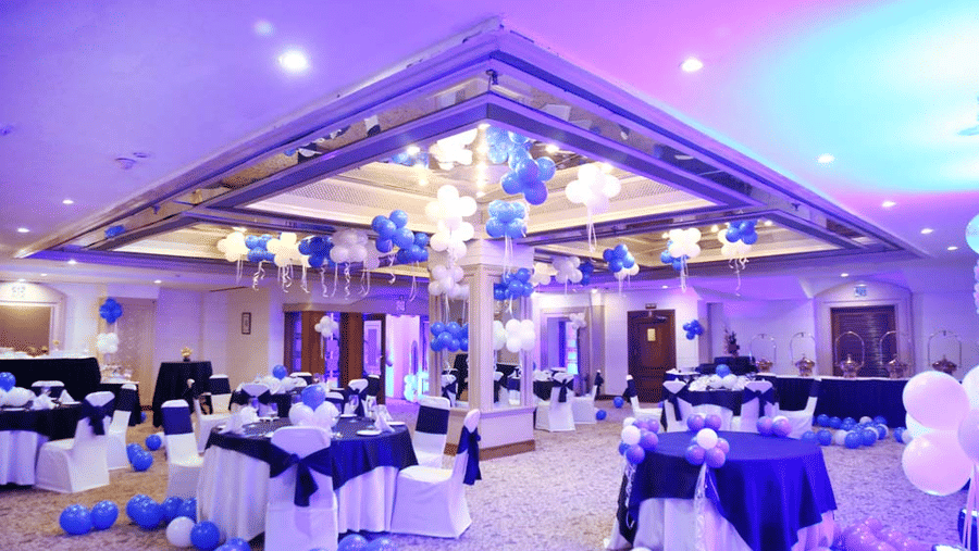 Banquet hall at The Bristol Hotel, Gurgaon with a mirrored ceiling reflecting balloons, round tables in navy and white linen, and buffet stations beyond.