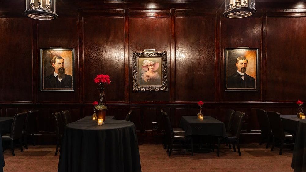 A dimly lit lounge with wooden walls, framed portraits, and intimate seating.- The Grand Hotel & Ballroom, McKinney