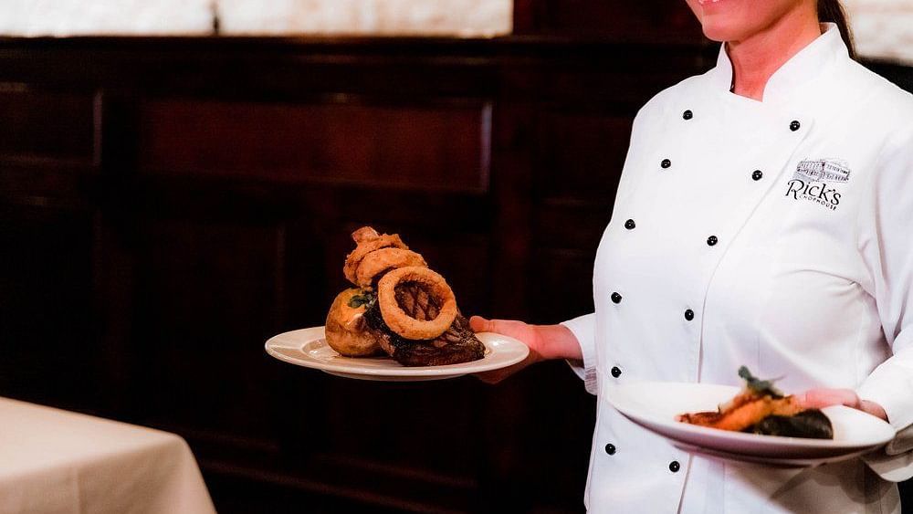 – A chef presenting a dish on a tray, offering a close-up view of the food in a restaurant setting.