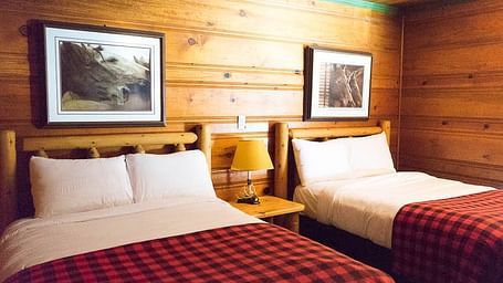 A wooden cabin with twin beds with photographs hung on the wall behind them at Shaver Lake Village Hotel.