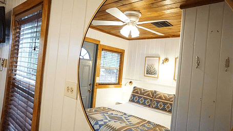 a double bed in a room with wooden ceilings reflecting off a round mirror hung on the wall in front of the bed at Shaver Lake Village Hotel.