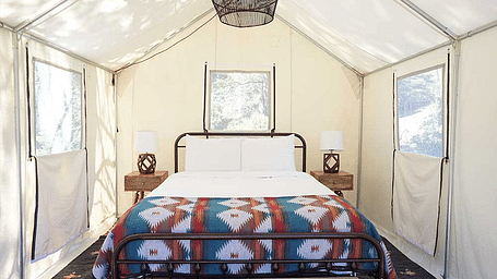 A tent with zip-down windows and a double bed placed in the middle at Shaver Lake Village Hotel.