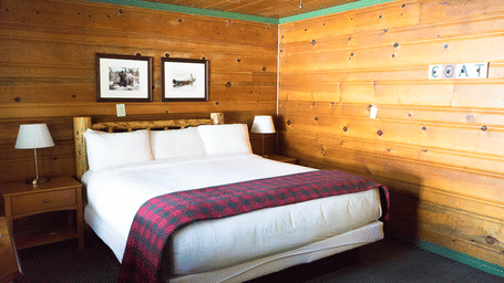 A double bed with a buffalo plaid duvet, and wall-mounted pictures in our wood-paneled lodging in Shaver Lake, CA.