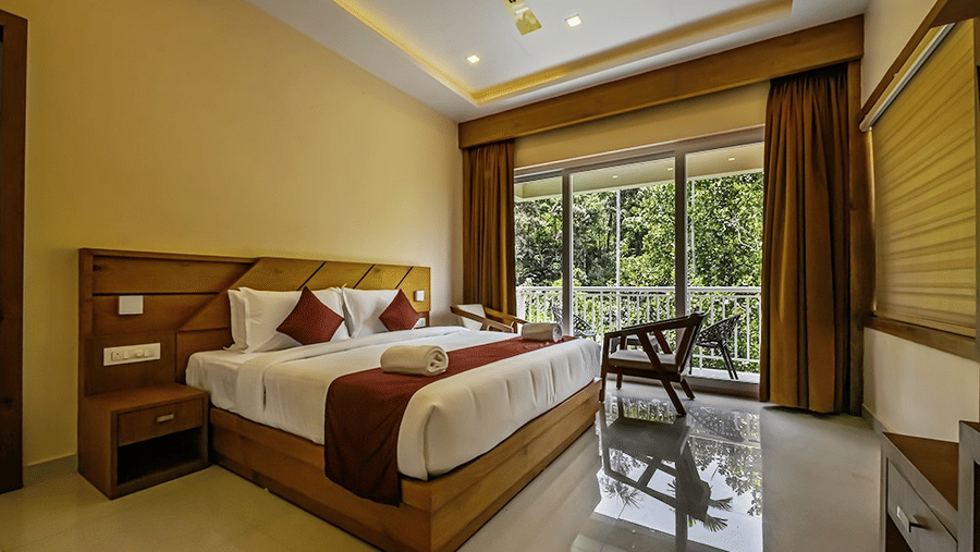 Full view of the Luxe Mountain View Cottage with a double bed in the centre overlooking the lush green views from the french windows at Aveda Mountains and Mist Resort and Spa, Munnar.