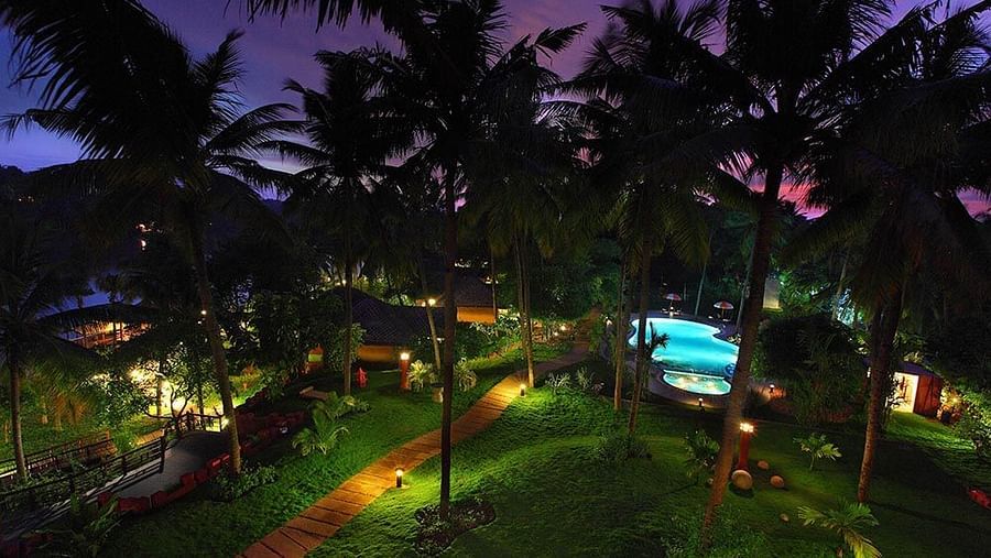 Facade view of Fragrant Nature Kollam, featuring a pool and surrounding trees at night