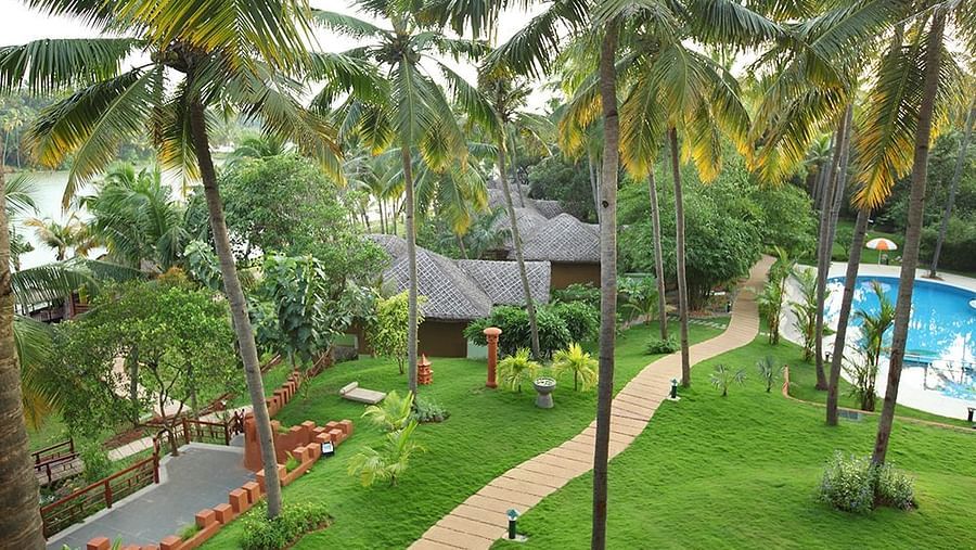 Facade view of Fragrant Nature Kollam, featuring a pool and surrounding trees.