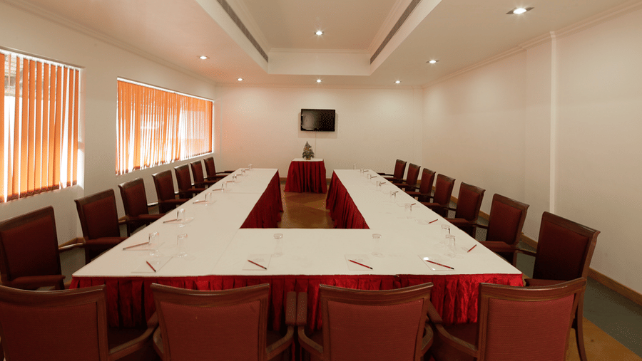 A conference room arranged with white tables in a rectangular layout surrounded by high-backed chairs | Le Pondy