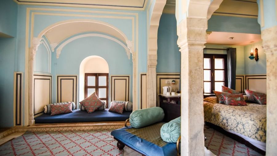 An interconnected suite  at Royal Heritage Haveli with a seating area featuring blue upholstery and a view into a bedroom through an archway.