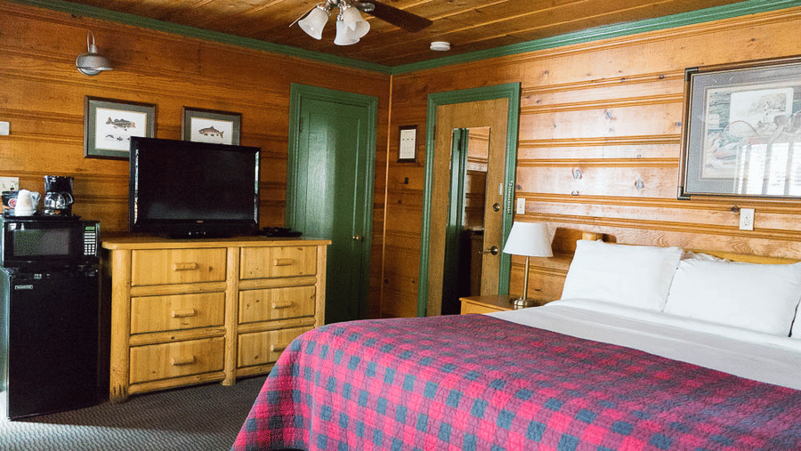 A room with a double bed, a wooden cabinet with a TV placed on it and a ceiling fan with a light at one of the best Shaver Lake places to stay.