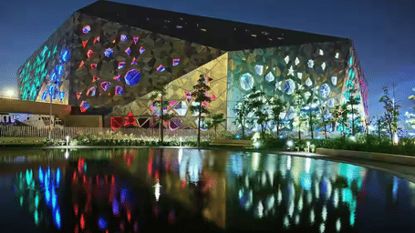 A large, colourful, illuminated building with a lake in front.