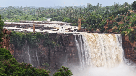 A large, wide waterfall surrounded by green trees.