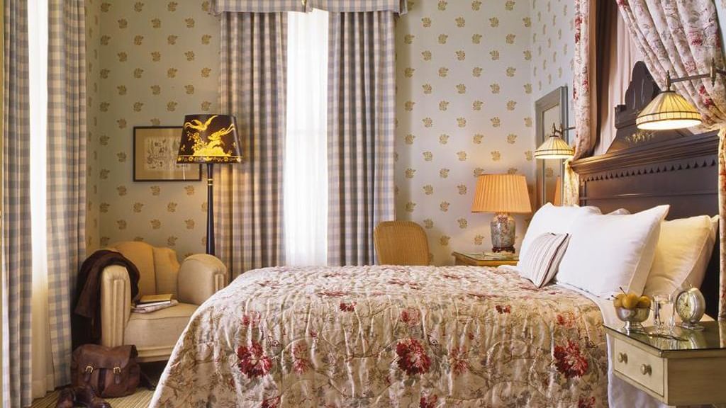 A beautifully decorated guest room at the Tallman Hotel with a cozy bed, armchair, and elegant furnishings.