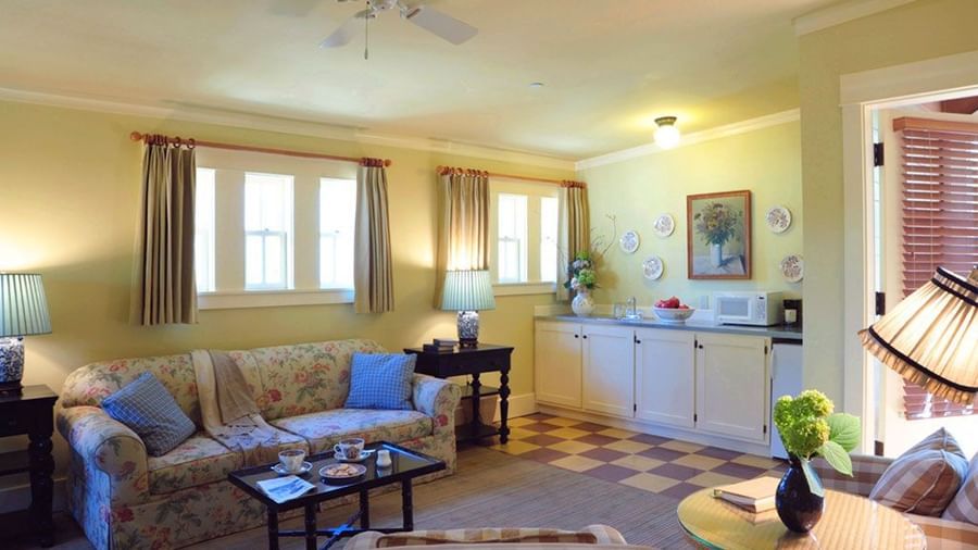A room at the Tallman Hotel shows a living space with a sofa, a table with apples, and kitchen cabinets.