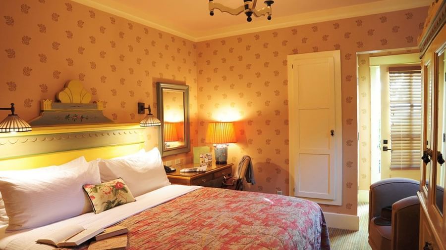 A bedroom at the Tallman Hotel contains a bed, nightstands with lamps, and patterned wallpaper.