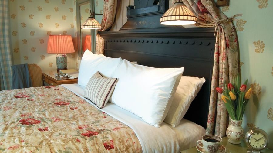 A bedroom at the Tallman Hotel contains a bed with a floral comforter and a dark wooden headboard.