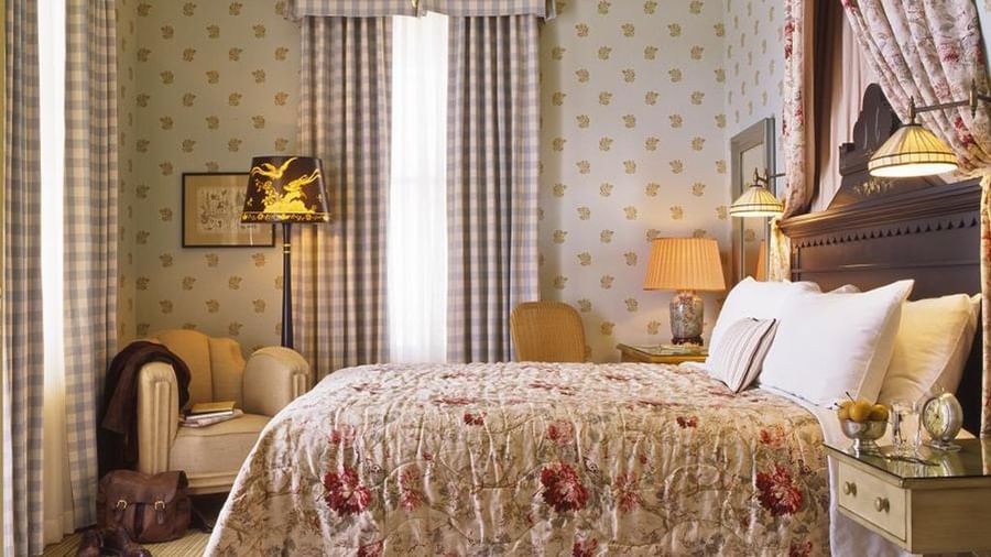 A beautifully decorated guest room at the Tallman Hotel with a cozy bed, armchair, and elegant furnishings.