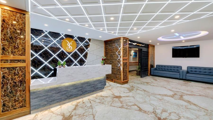 The lobby area at the Yashshree Sikkim Blossom in Gangtok, with a modern interior, two sofas, a wall mounted television and an entrance into the hotel.