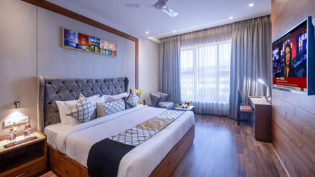 Executive room with a queen-sized bed, grey padded headboard, wall-mounted TV, large window, and minimalist decor.