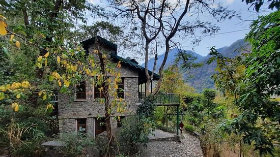 Facade view of Glasshouse on the Ganges amidst the nature with mountains and clear blue sky in the background.