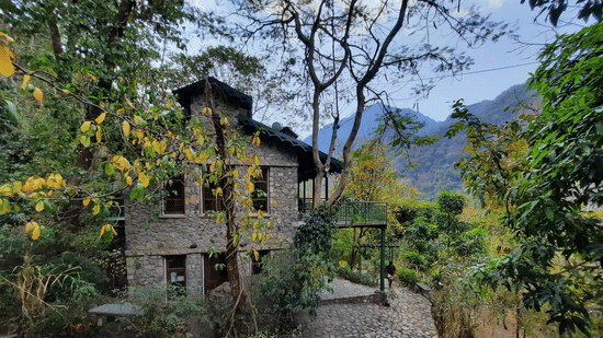 Facade view of Neemrana's Glasshouse on the Ganges amidst the nature with mountains and clear blue sky in the background.