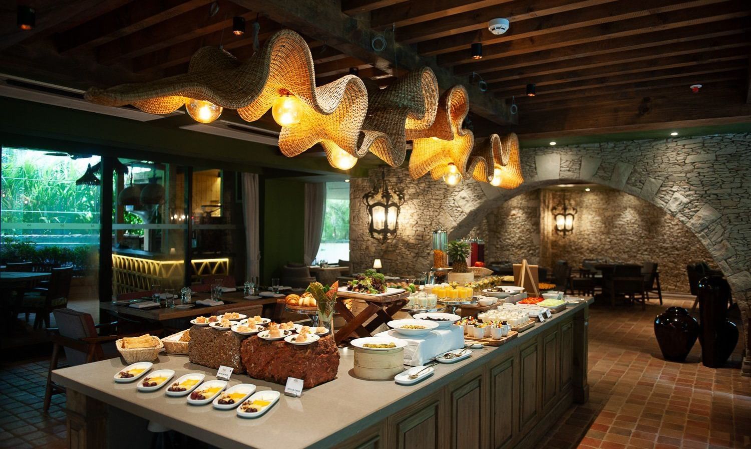 A lavish breakfast buffet spread at the Mila Restaurant at The Evren, Vagator, featuring a variety of dishes on display under the woven light fixtures.