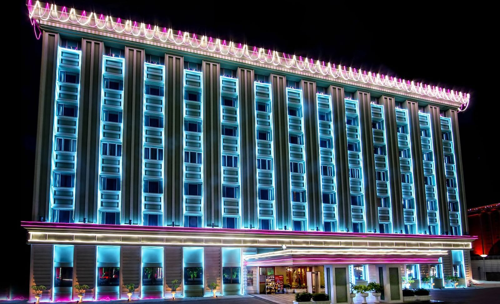 The facade of a hotel illuminated with blue neon lights at night - Tara, Comfort Hotel in Hyderabad - Ramoji Film City.