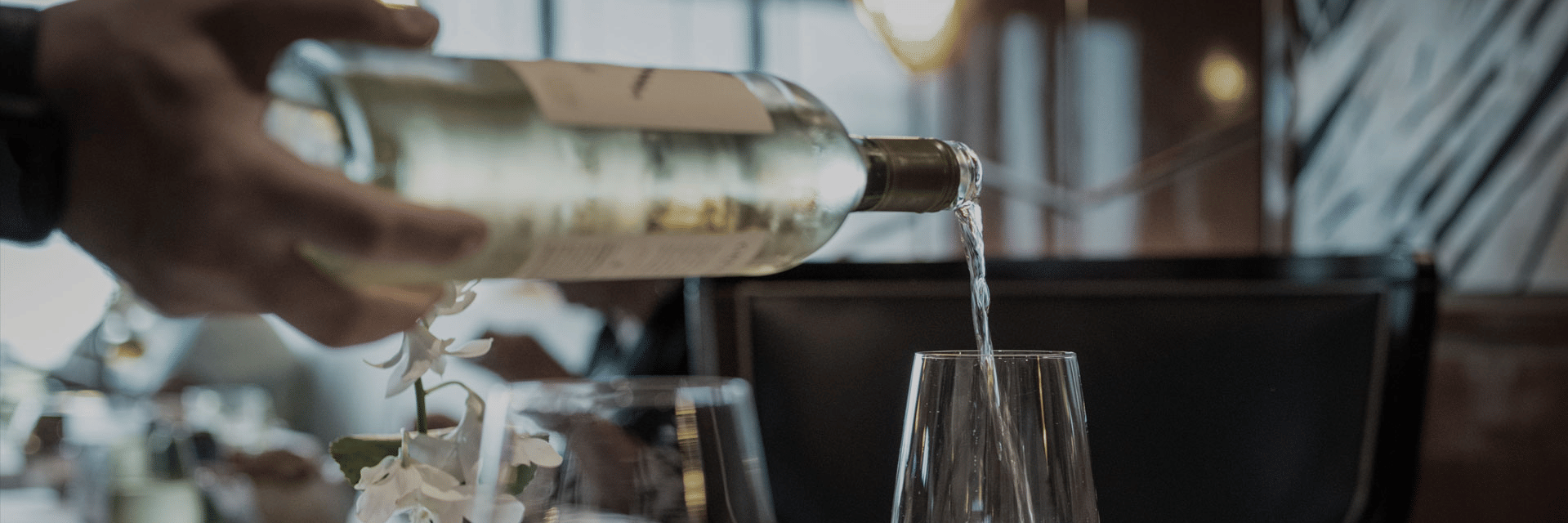 Close-up of a hand pouring white wine from a bottle into a clear glass.