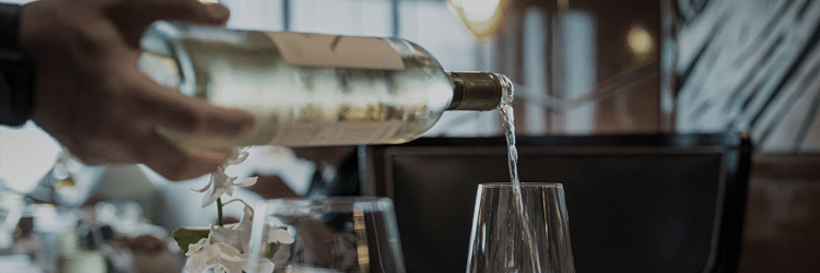 Close-up of a hand pouring white wine from a bottle into a clear glass.