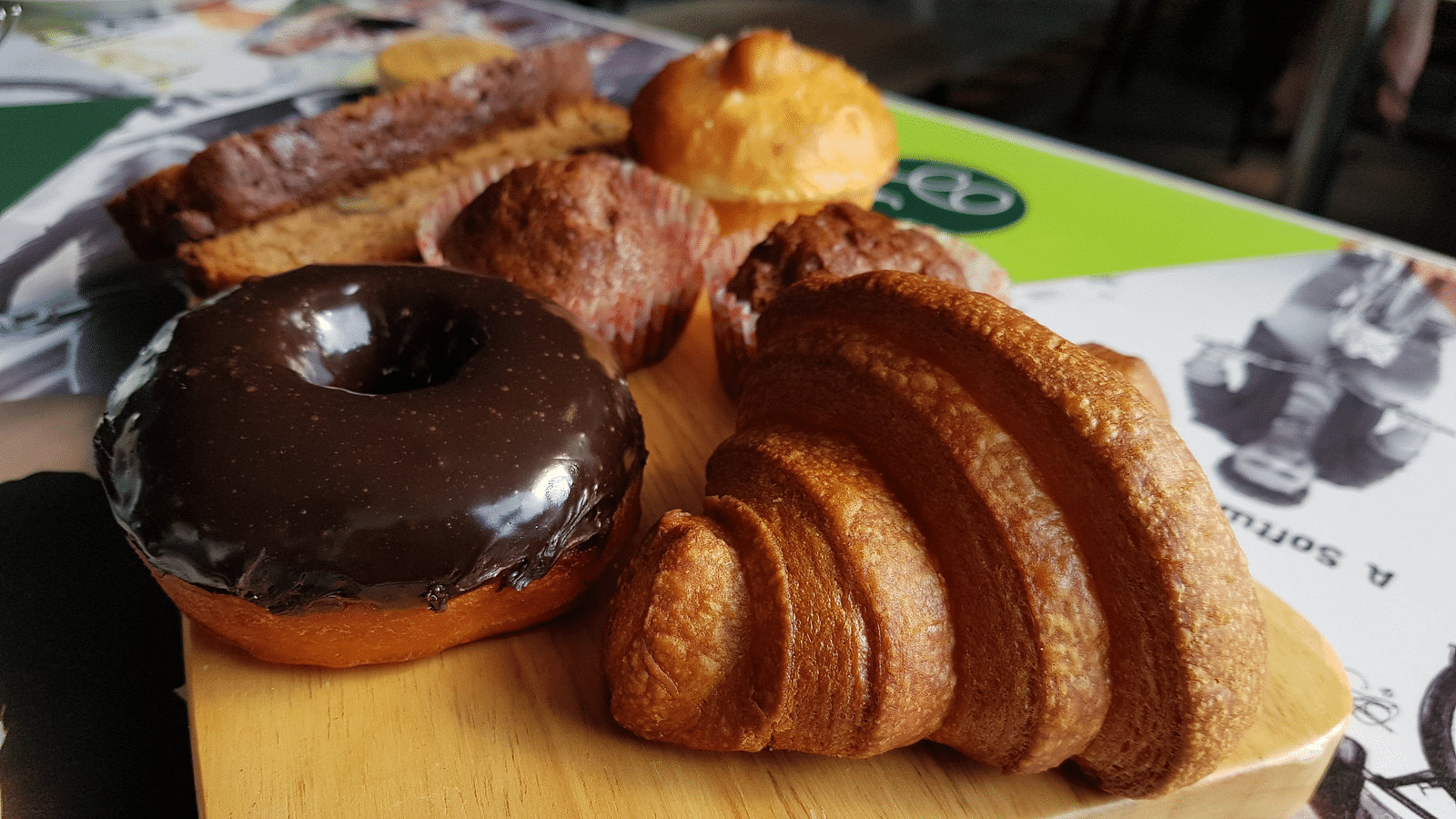 A variety of pastries on a wooden board, including a chocolate-glazed donut, a croissant, and several other baked goods