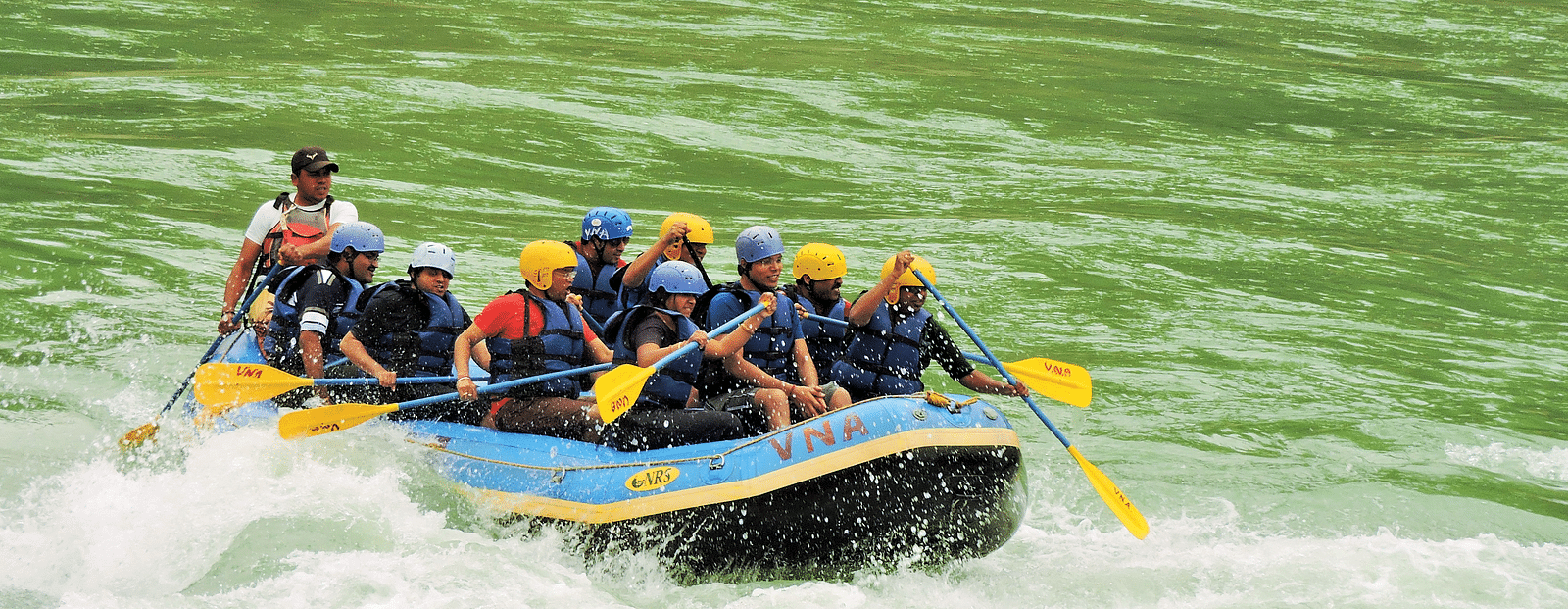 A group of people rafting on a single raft in a rushing river, splashing water around them. 