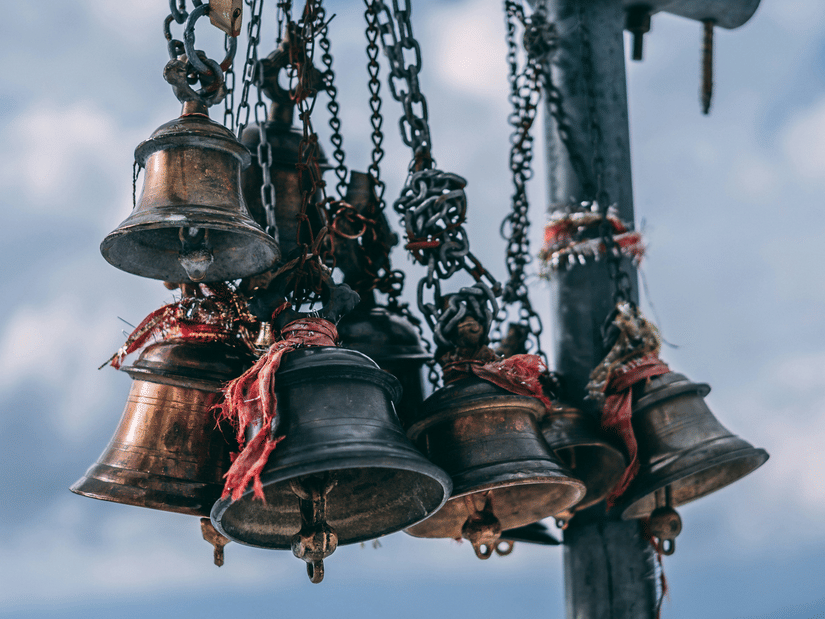 Traditional metal temple bells hanging at a sacred site, symbolising spirituality and cultural heritage.