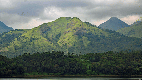 Rolling green hills near a hill under dramatic clouds in Wayanad