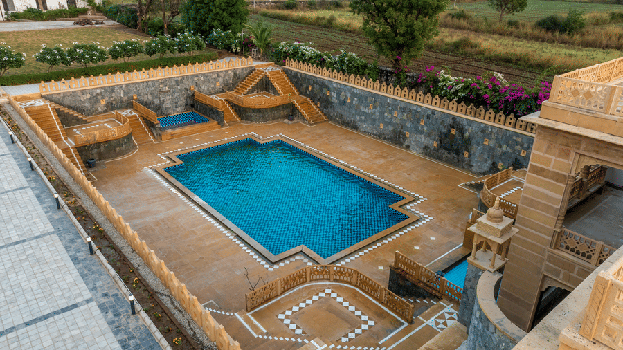 High-angle view of the swimming pool at EsthereaRaj Leela, Ranakpur, surrounded by stone decks and architectural stairs.