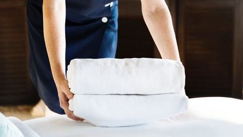 An image of a housekeeping person lifting the clothes for laundry from the bed