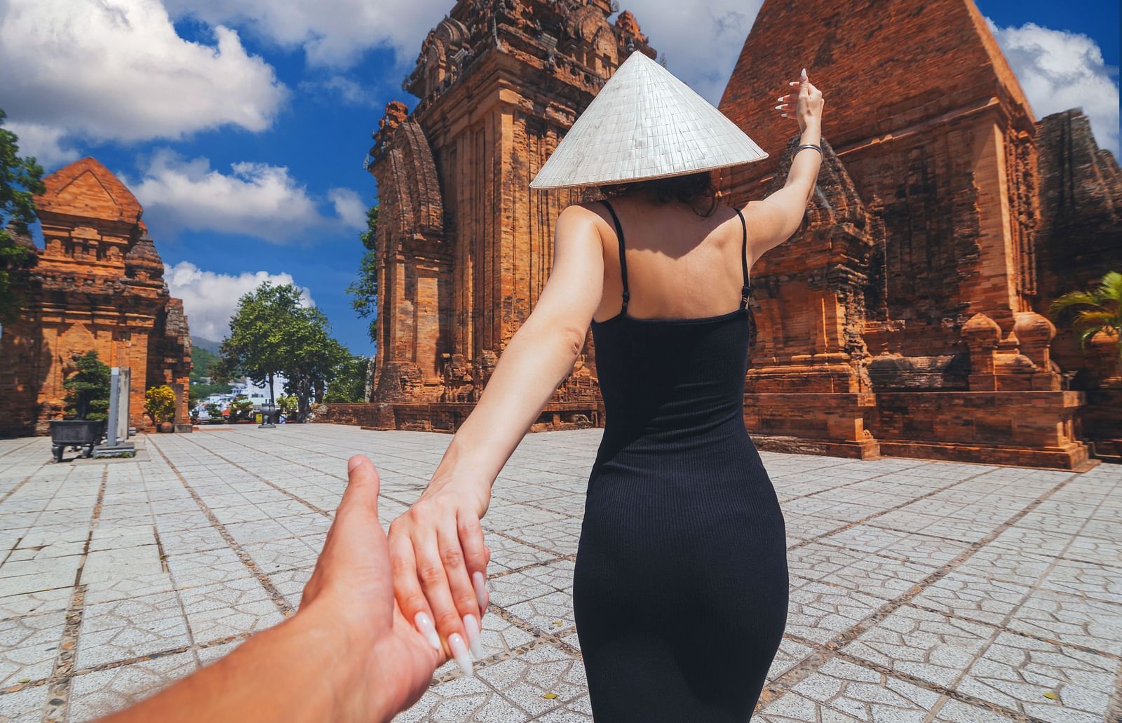 Back view of a person in a hat, holding hands, with tiered architecture in the background.