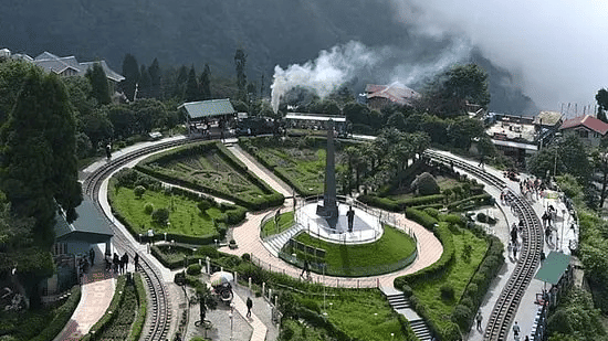 Aerial view of the Batasia Loop’s circular railway track and garden, with a steam engine puffing smoke in the distance.