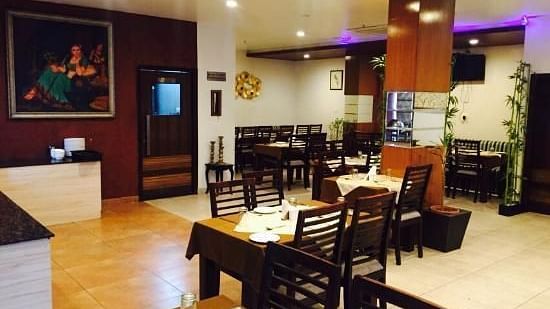 An elegantly set dining area with wooden chairs and tables, under ambient lighting and a painting on the wall - TGI Apple Inn, Jaipur 