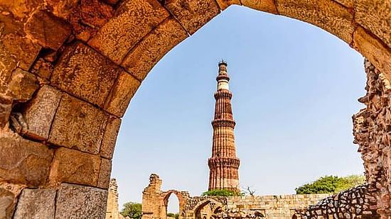 Qutub Minar framed through a stone archway, showcasing the historic Indo-Islamic architecture against a clear blue sky.
