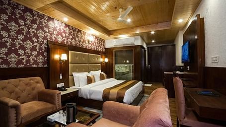 A expansive hotel room with a king size bed, two armchairs, and a small table in the centre | DLS La Serene Manali
