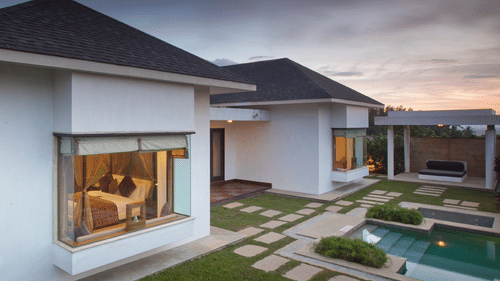A modern resort villa at dusk with a private pool and a landscaped yard with stepping stones, located at The Serai Chikmagalur.