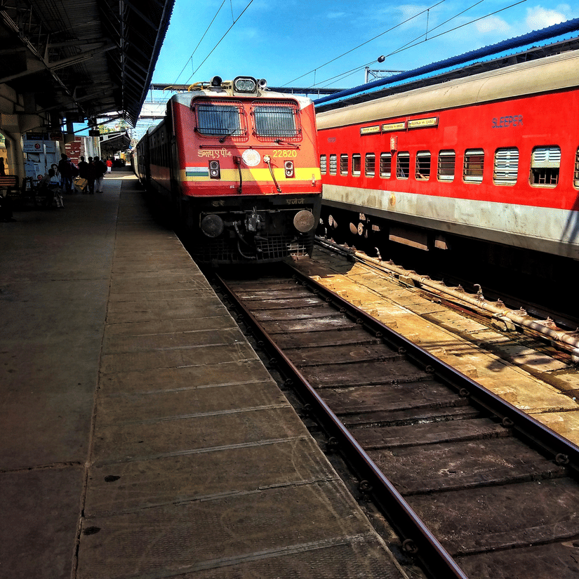 A view of a train station with a train parked on the right hand side and another train taxing to a stop as seen during day time
