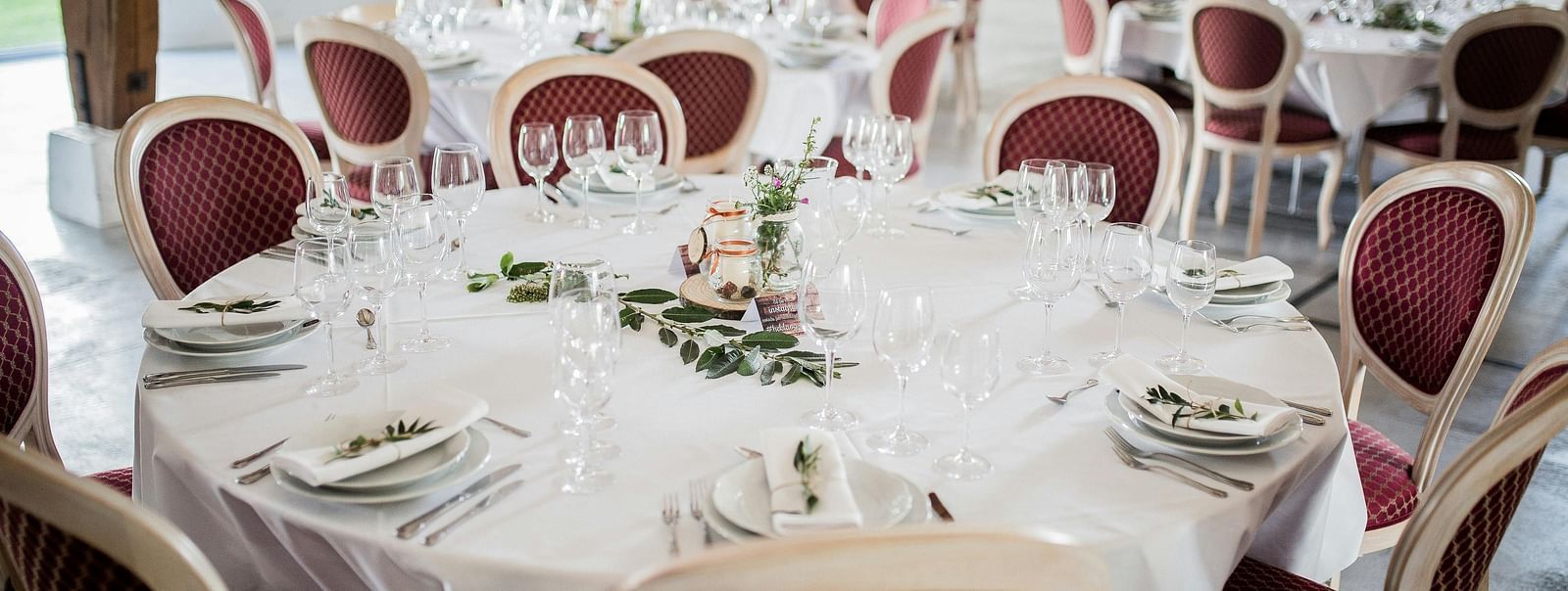 image of a round shaped table covered with a white cloth in a banquet hall with maroon coloured cushioned chairs surrounding the table