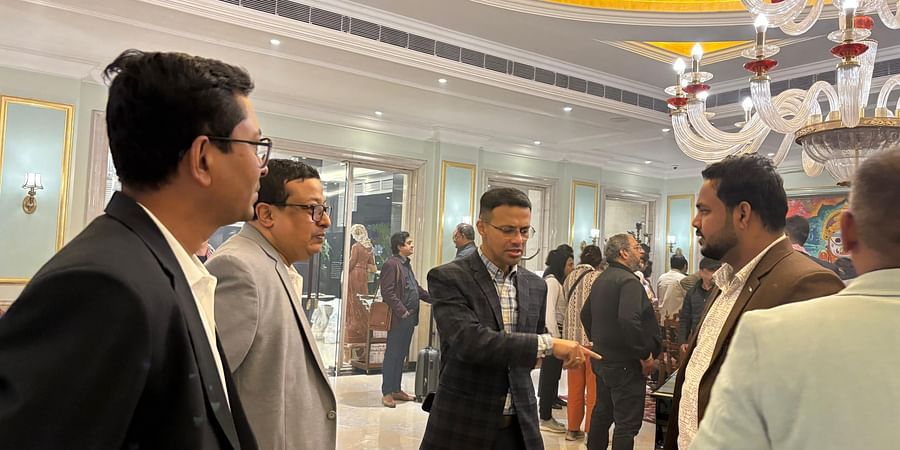 A group of men in formal attire engaged in conversation at an indoor event with a chandelier and decorated ceiling.