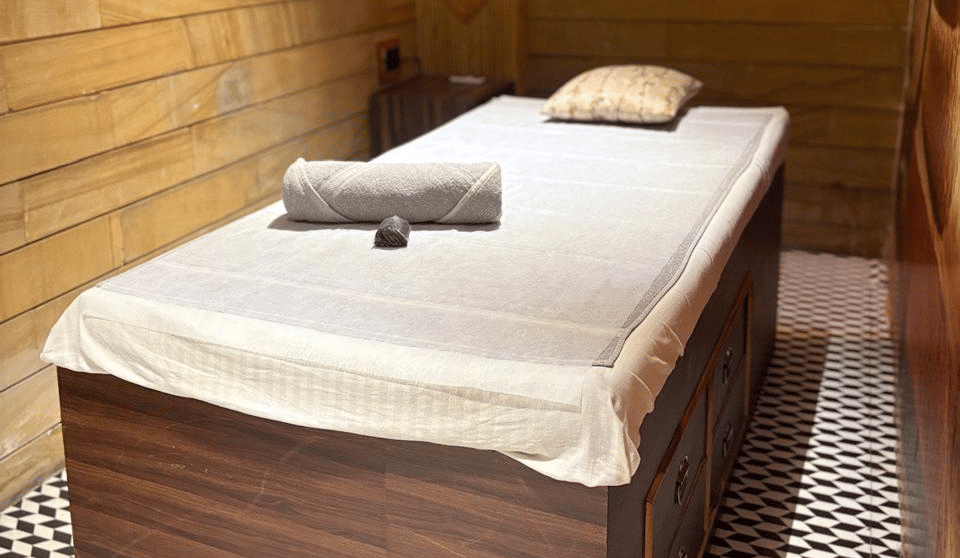 Spa treatment bed with white linen, a rolled towel and a cushion against warm wood panelling