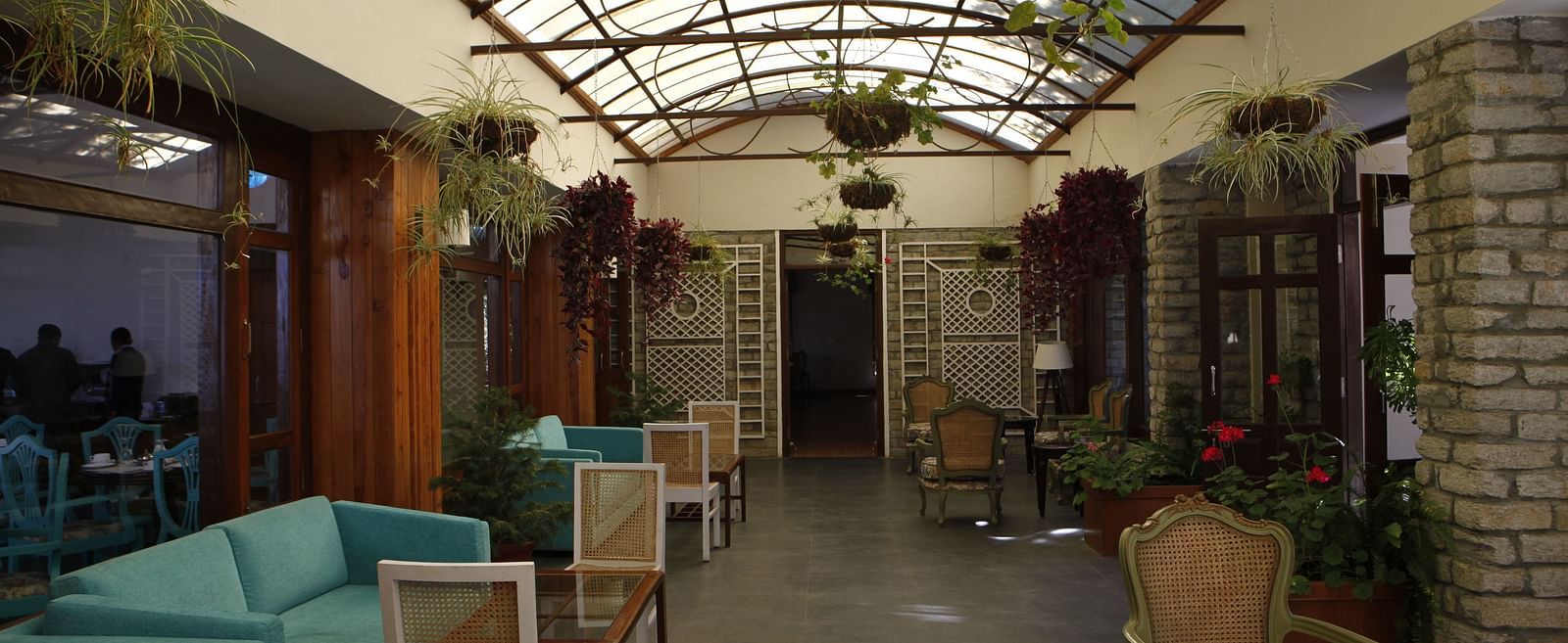 A close up shot of a lounge in Almora with a teal sofa, chairs, and a transparent ceiling from which potted plants are hung - BluSalzz Escapade - Anant Rasa Resort
