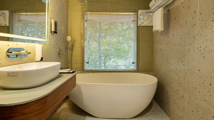 A tiled bathroom featuring a white bathtub, a wash basin and a mirror, a shower, fresh towels on a shelf, a big window with blinds, and an exhaust fan | Summit by the Ganges Beach Resort & Spa, Rishikesh