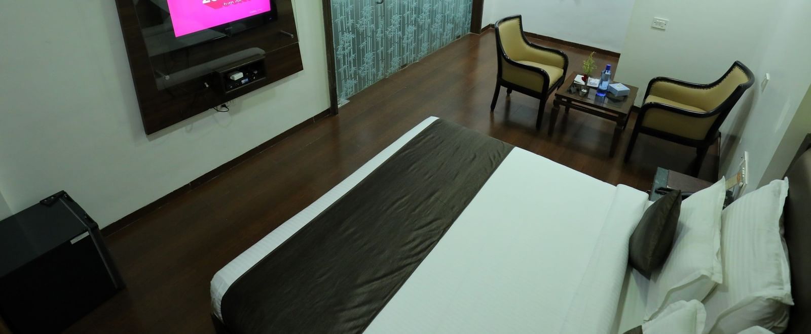 A top angle of a bedroom at Krushnai Resort with a bed, two chairs and a wall-mounted television.
